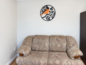 Ein modulares Sofa mit gemustertem Stoff, ein an der Wand befestigtes Vogelkunstwerk und eine dunkel gefärbte Tür.