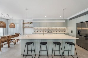 Eine moderne Küche mit einer zentralen Kochinsel, Barhocker und einem Edelstahlkühlschrank.