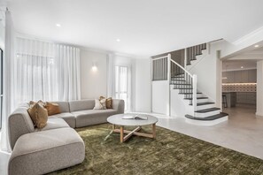 Ein modernes Wohnzimmer mit einer Eckcouch, einem runden Couchtisch und einer Treppe, die in ein Obergeschoss führt.