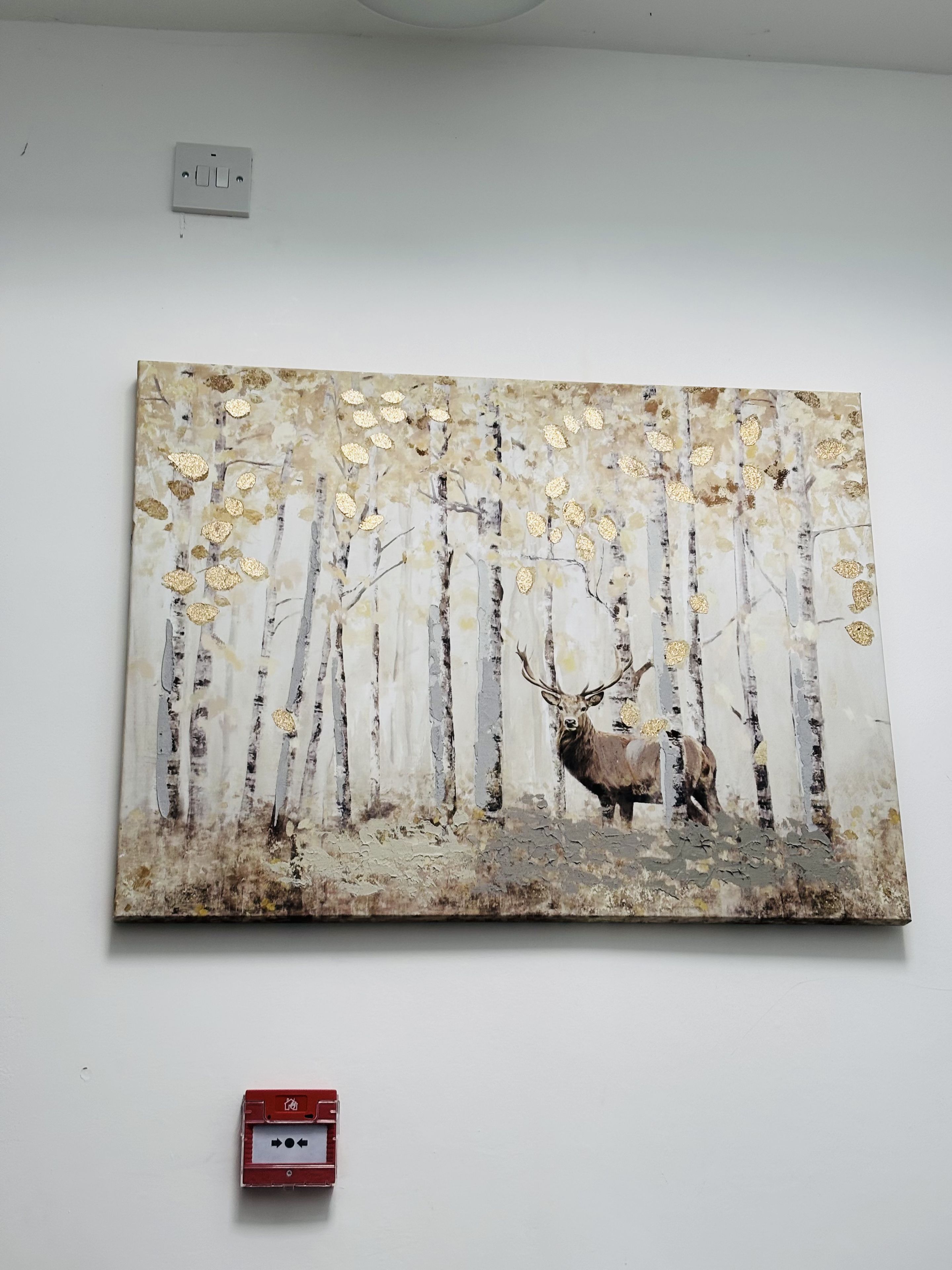A painting of a forest scene with a deer, mounted on a white wall.