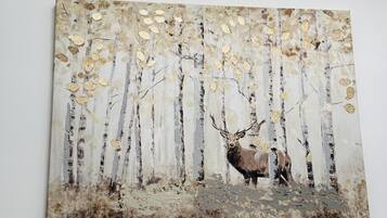 A painting of a forest scene with a deer, mounted on a white wall.