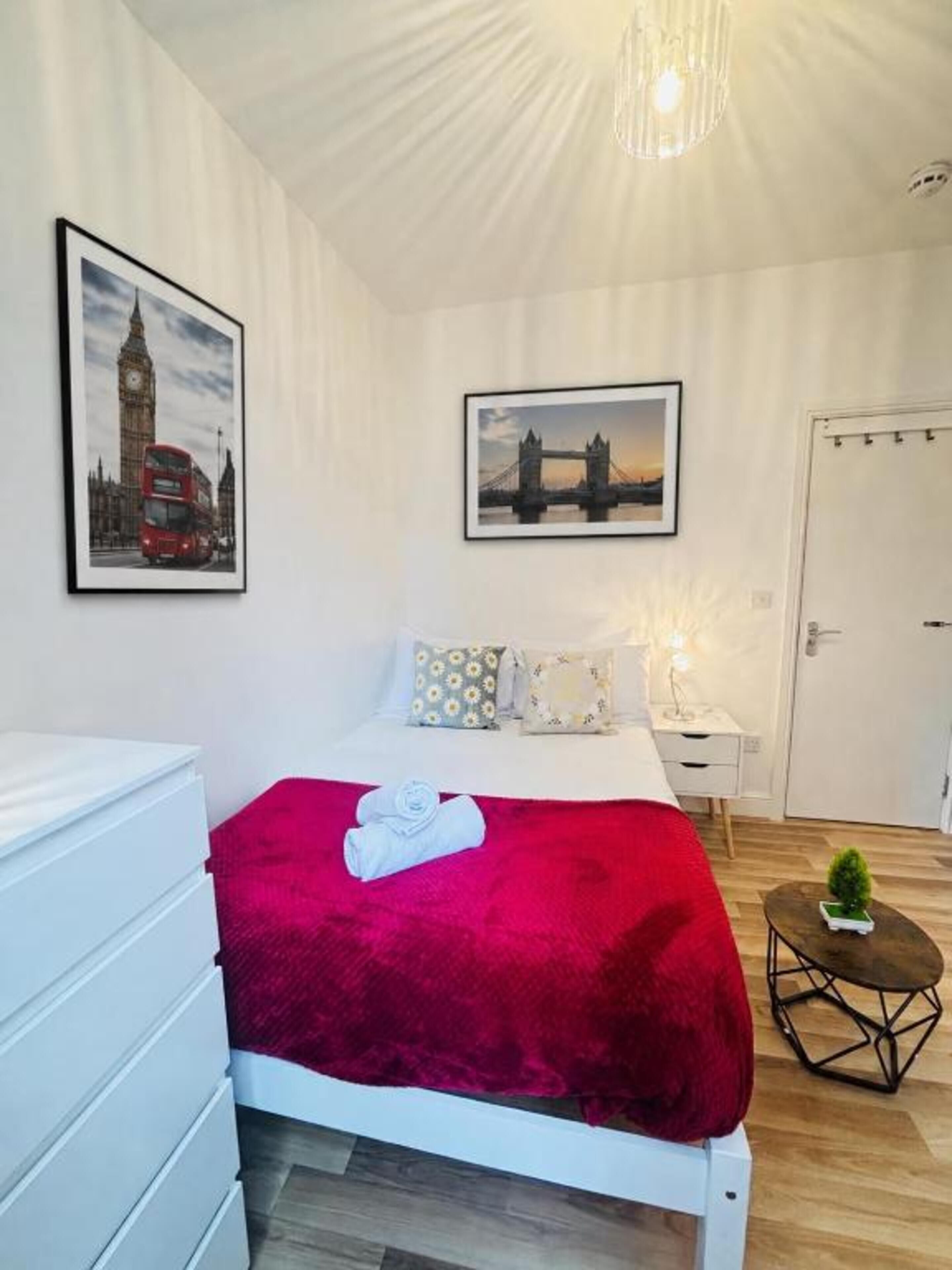 A bedroom with a bed, a dresser, a nightstand, a lamp, and two framed pictures on the wall.