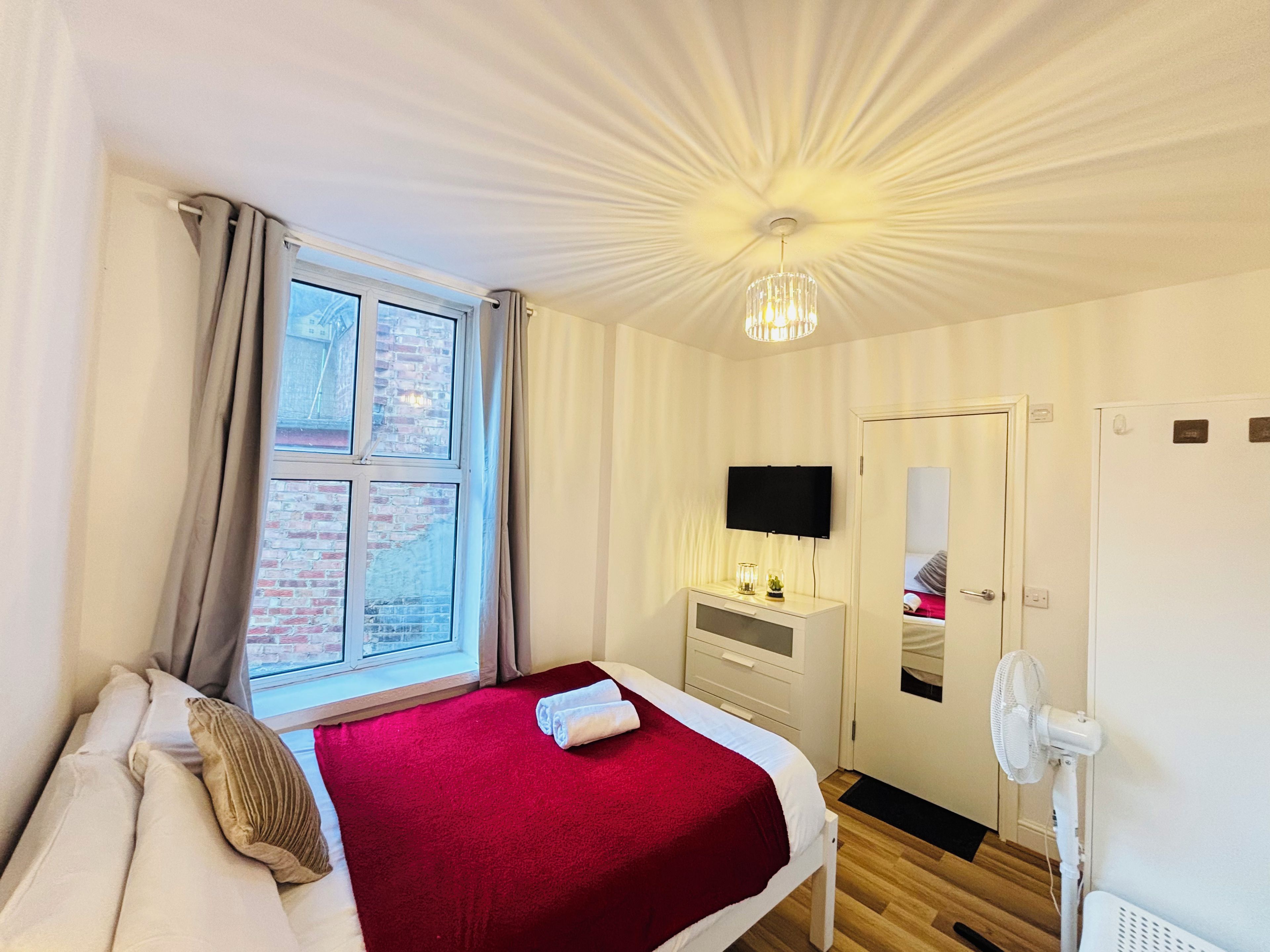 Een hotelkamer met een bed, een televisie, een bureau, een spiegel en een raam met gordijnen.