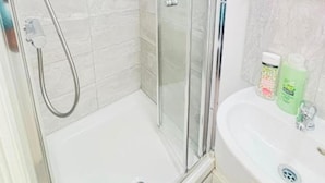 Casa de banho com cabine de chuveiro de vidro, lavatório branco e espelho em cima.