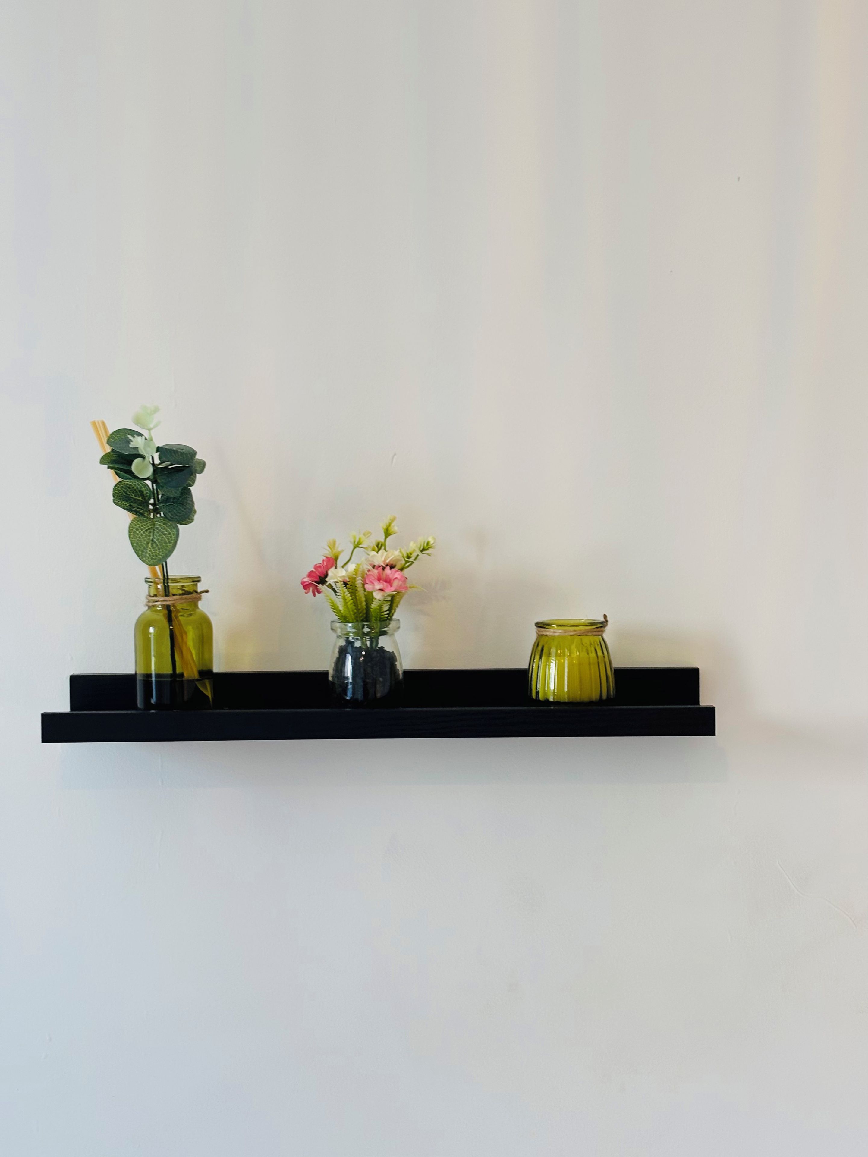 A black shelf with three glass vases containing plants and flowers.