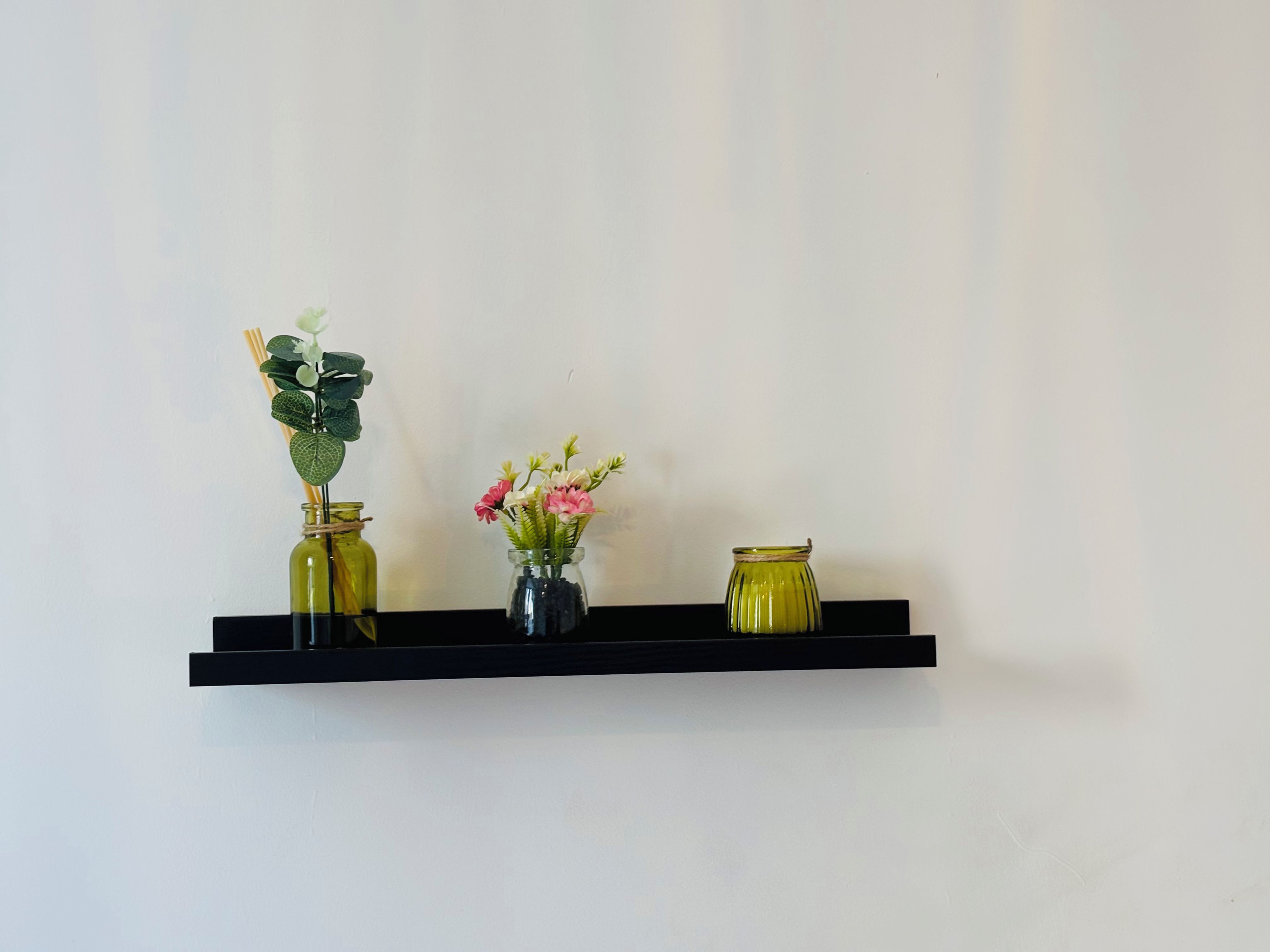A black shelf with three glass vases containing flowers.