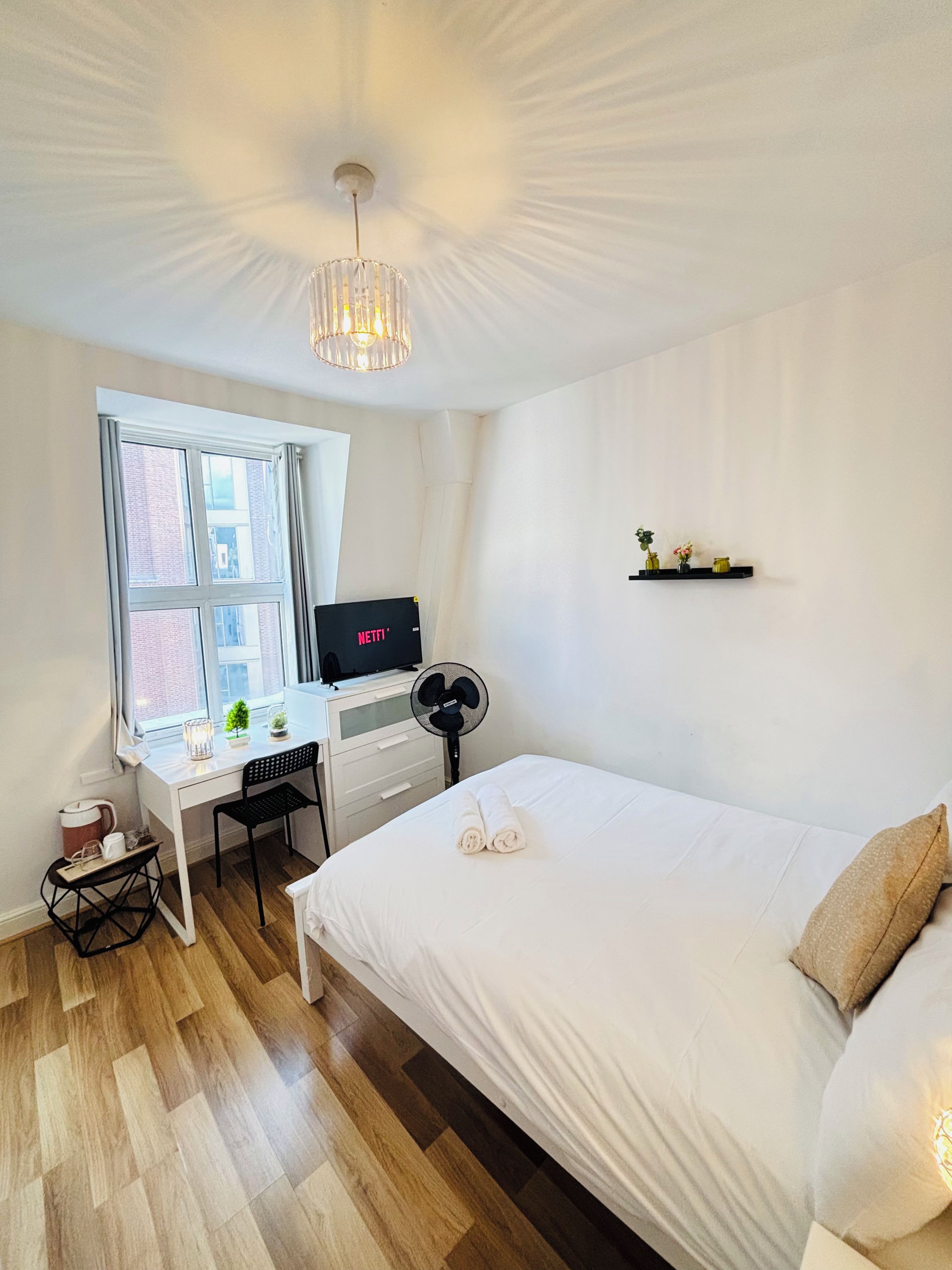 A hotel room with a bed, a desk with a computer, a window, and a ceiling fan.