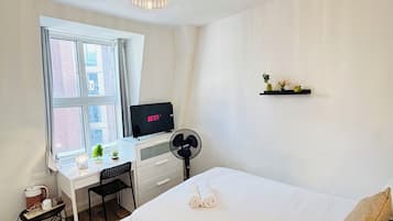 A hotel room with a bed, a desk with a computer, a window, and a ceiling fan.