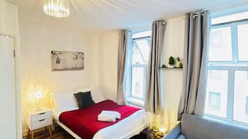 A hotel room with a bed, a sofa, a nightstand, a chandelier, and a window with curtains.