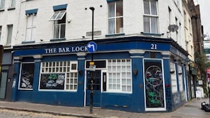 Um edifício com fachada azul e branca, um letreiro que diz 'The Bar Lock' e o número '21' no canto.
