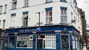A building with a blue and white facade, a sign reading 'The Bar Lock,' and a number '21' on the corner.