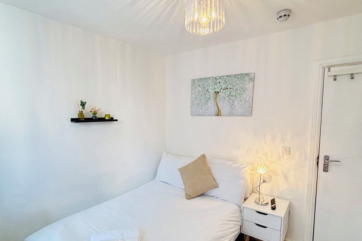 Un dormitorio con cama, mesitas de noche, una puerta, una lámpara en el techo y un estante en la pared con objetos decorativos.
