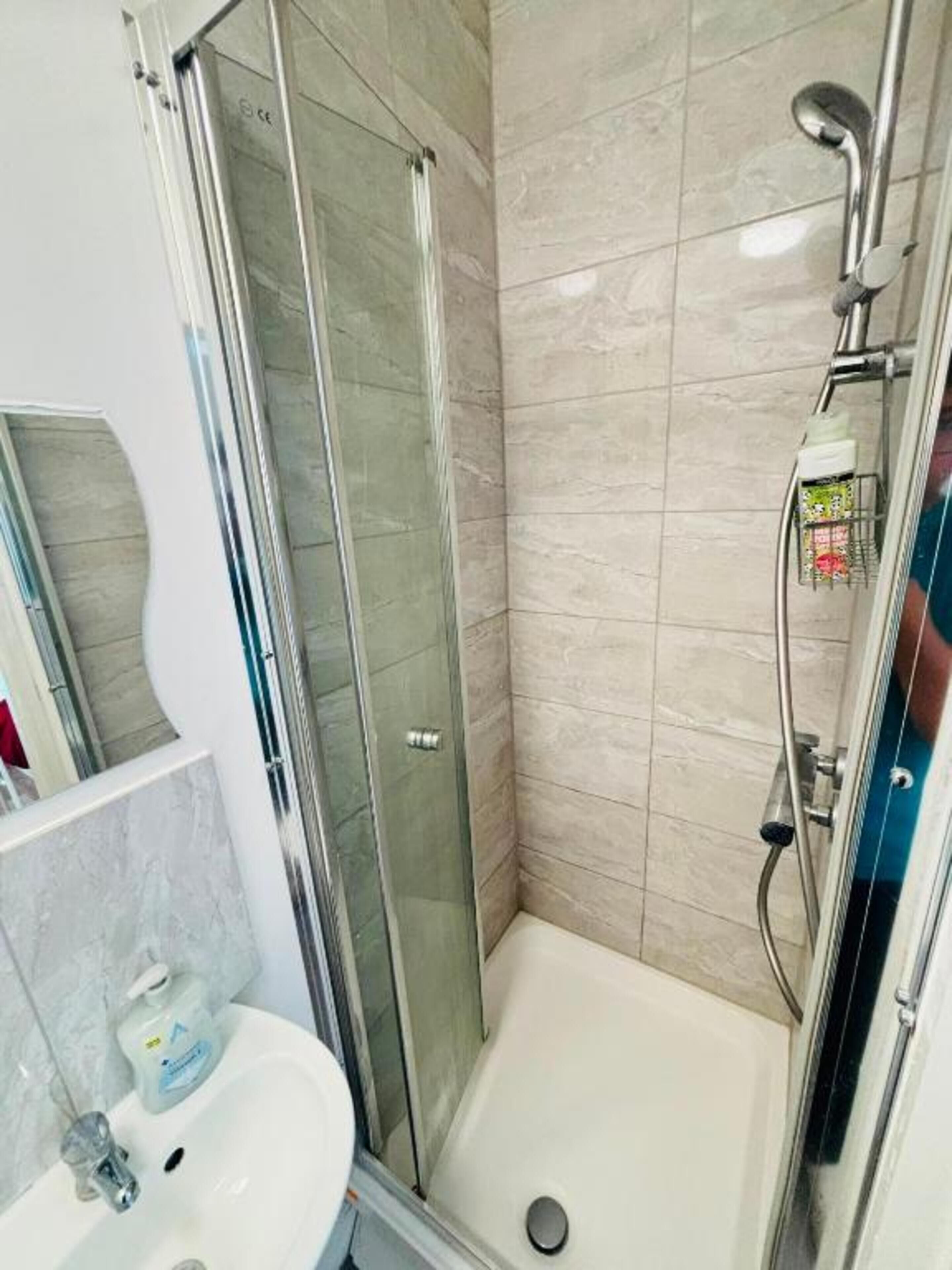 A bathroom with a glass-enclosed shower, a white sink, and a tiled wall.