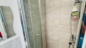 Casa de banho com chuveiro em cabine de vidro, lavatório branco e parede revestida a azulejos.