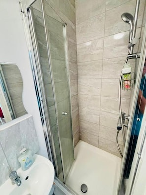 A bathroom with a glass-enclosed shower, a white sink, and a tiled wall.