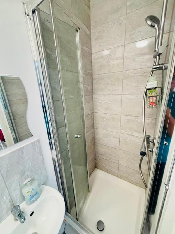 Un baño con ducha de vidrio, un lavamanos blanco y pared con azulejos.