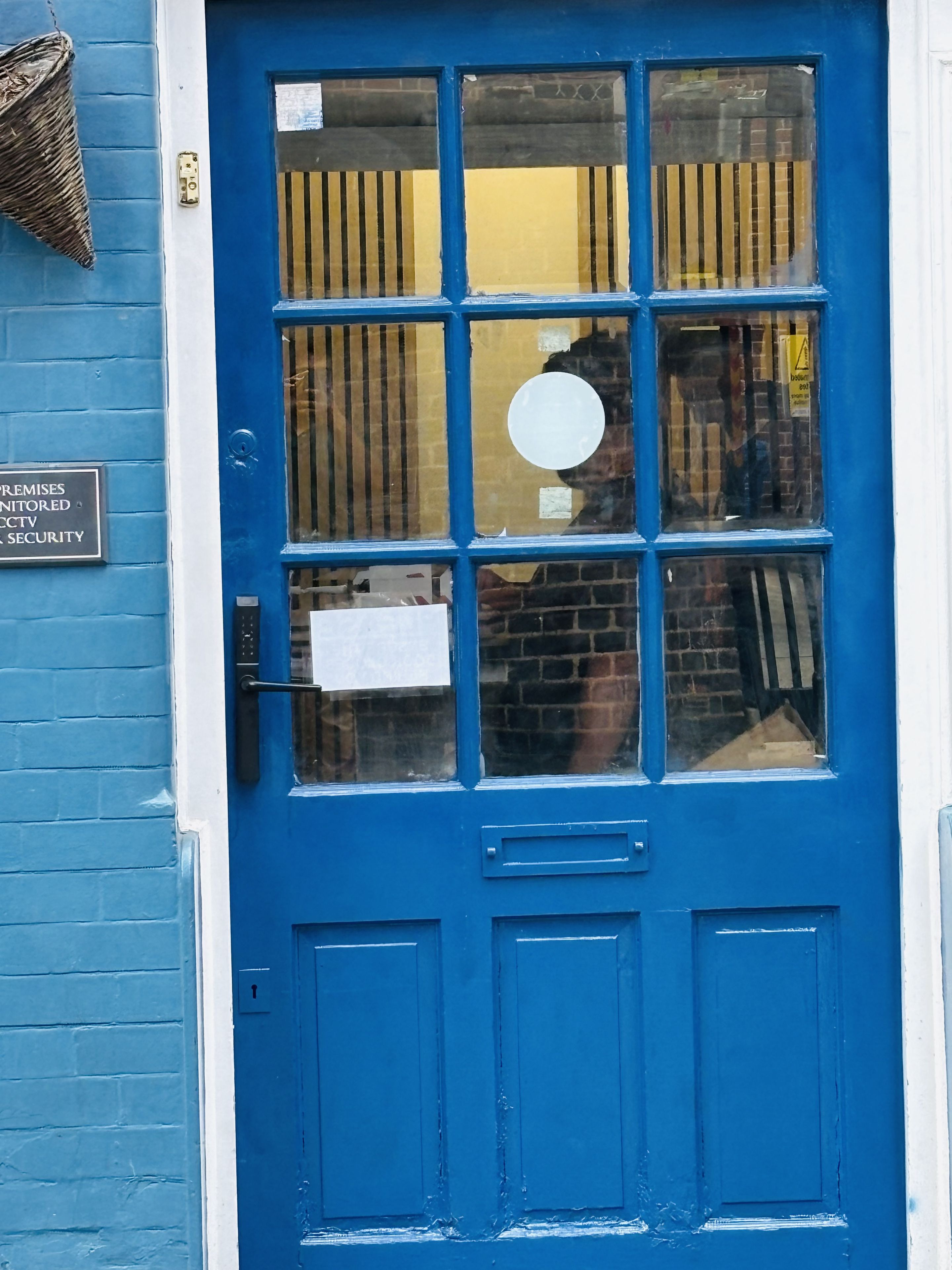 A blue door with a security sign, a keypad, and a window with a view of the street.
