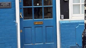 Uma porta azul com uma janela acima, uma placa na parede e uma caixa de correio à direita.