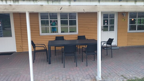 An outdoor seating area with a table and chairs, a covered patio, and a building with windows and a door. - Holiday home with large garden by Limfjord (Storvorde)