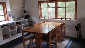 A dining area with a wooden table and chairs, a kitchen area with cabinets and appliances, and a window with a view of greenery. - Holiday home with large garden by Limfjord (Storvorde)