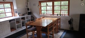 Ein Essbereich mit Holztisch und Stühlen, ein Küchenbereich mit Schränken und Geräten sowie ein Fenster mit Blick auf Grünflächen.
