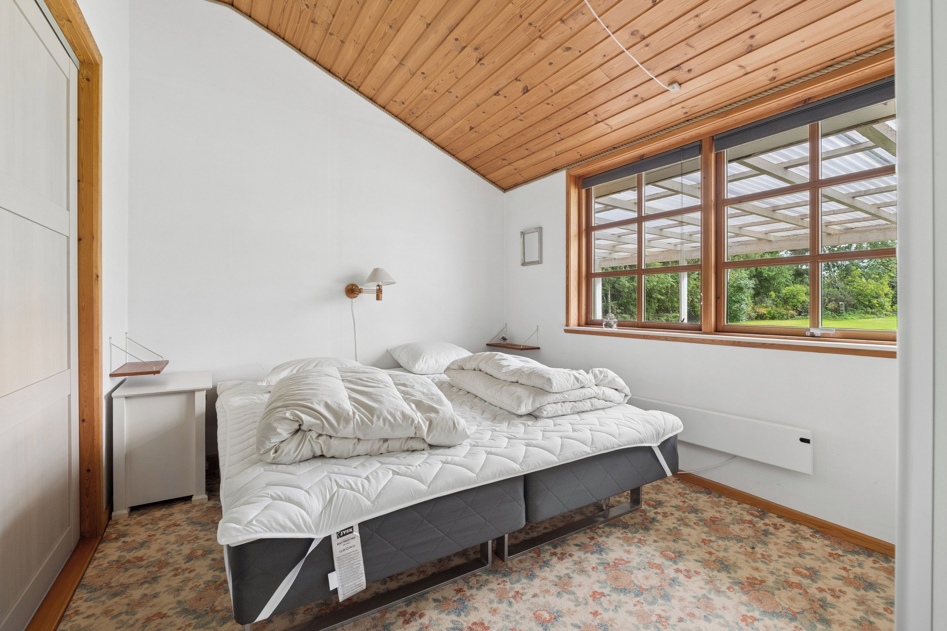 A bedroom with a bed, a bedside table, a lamp, a window, and a radiator.