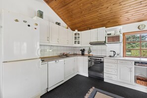 A kitchen with white cabinets, a stove, a microwave, and a window with a view of greenery. - Holiday home with large garden by Limfjord (Storvorde)