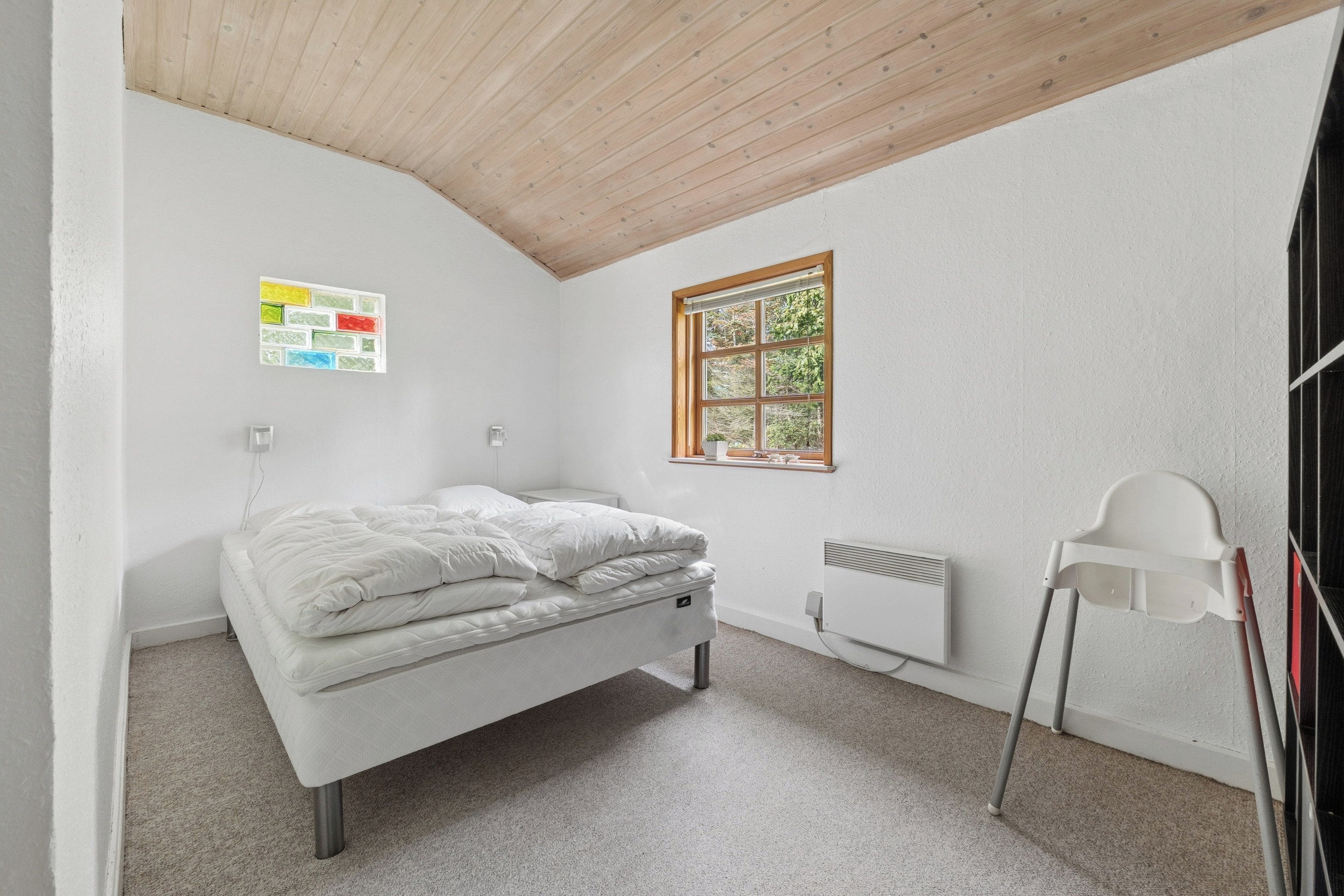 Un dormitorio con una cama individual, un radiador, una ventana con vistas a árboles y una silla blanca.