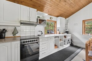 Keittiössä on valkoiset kaapit, liesi ja ikkuna, josta avautuu näkymä vehreään maisemaan.