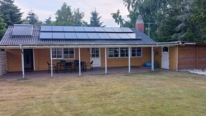 A single-story building with a covered patio area, a solar panel array on the roof, and a fenced yard. - Holiday home with large garden by Limfjord (Storvorde)