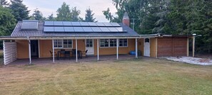 Ein eingeschossiges Gebäude mit überdachter Terrasse, einer Solaranlage auf dem Dach und einem umzäunten Garten.