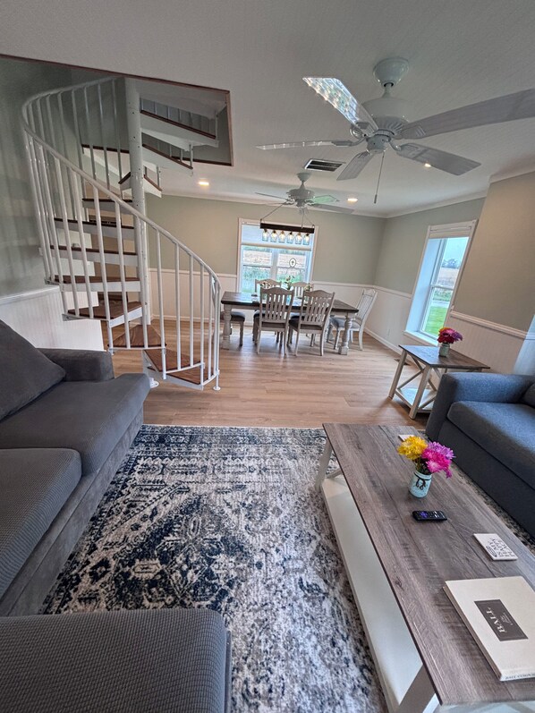 A modern living room with a staircase, a dining area, and a large window providing natural light.