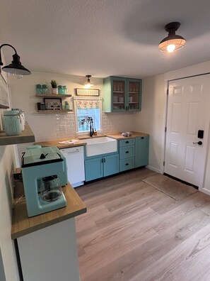 A kitchen with teal cabinets, a white sink, and a coffee maker on the counter.