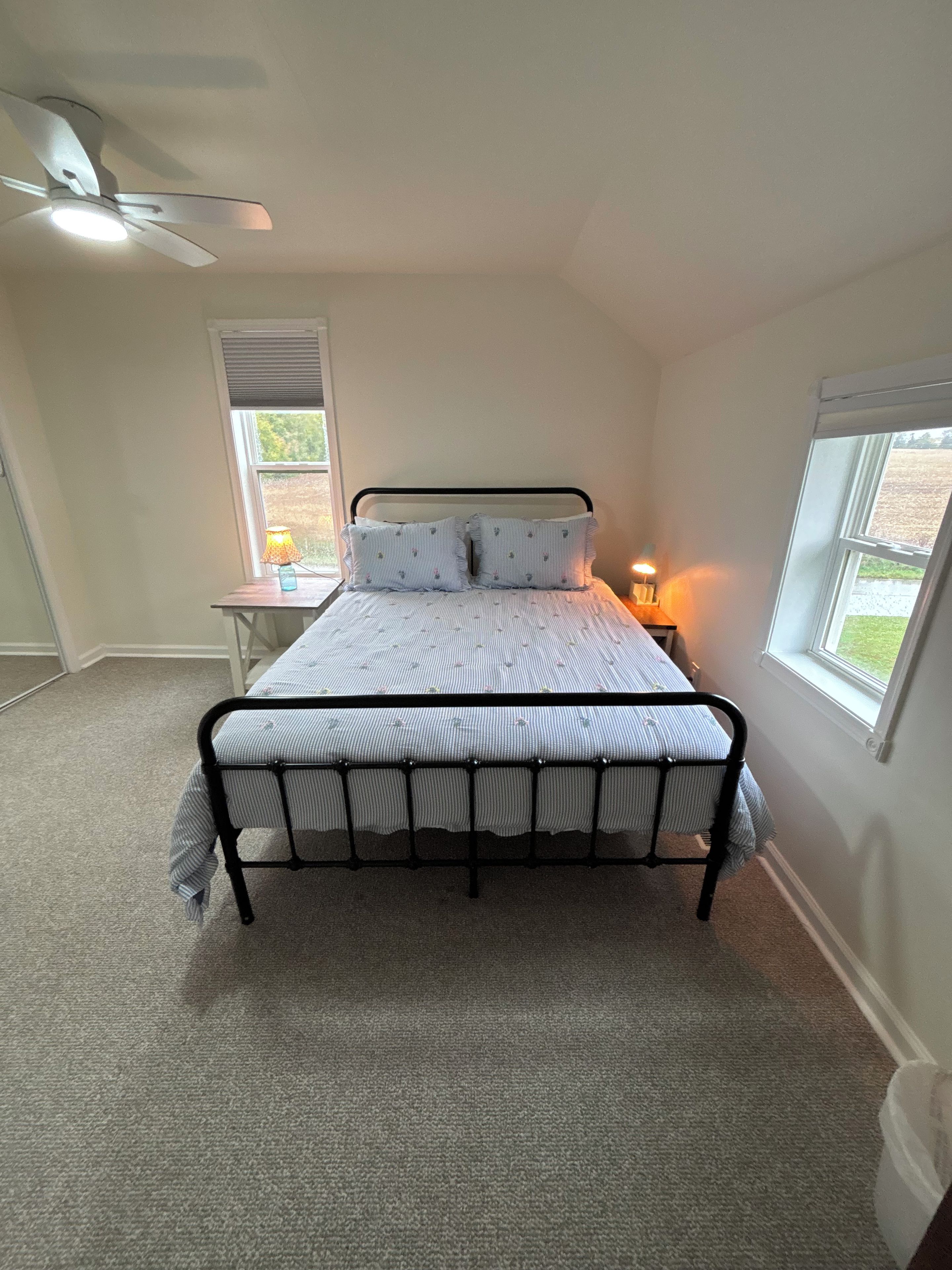 A bedroom with a bed, a nightstand, a lamp, a window, and a ceiling fan.