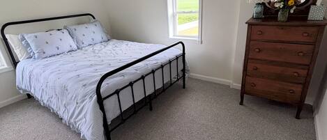 A bedroom with a single bed, a dresser, a window, and a mirror.