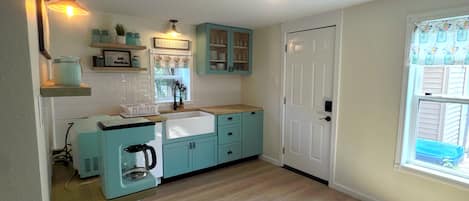 A kitchen with light blue cabinets, a white sink, and a coffee maker. There is a window with a view of the outside.
