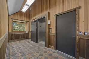Ein Korridor mit Steinmuster-Boden, Holzwänden, einem Fenster mit Aussicht und zwei Aufzügen.