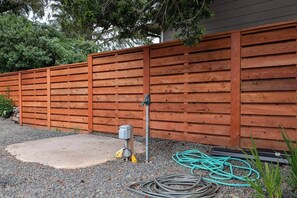 Ein Holzzaun, eine Beton-Terrasse und ein Gartenschlauch auf Kies.