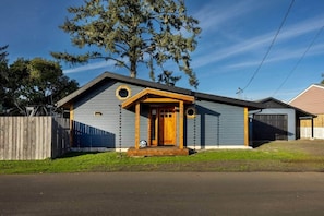 A single-story house with a front porch, a garage, and a fenced yard. - Cozy Crabin - Pet Friendly, Trailer Hook Up, Boat parking, Bay Access (Waldport)
