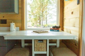 A wooden interior with a white table, a coffee maker, and a window with a view of trees. - Cozy Crabin - Pet Friendly, Trailer Hook Up, Boat parking, Bay Access (Waldport)