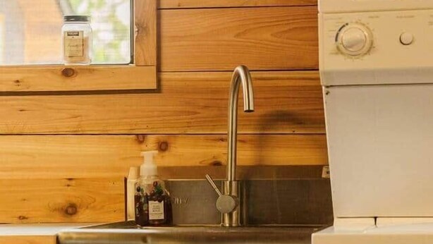 Uma cozinha com pia de aço inoxidável, armários de madeira, uma janela e uma placa com a inscrição 'Lar Doce Casa na Kombi'.