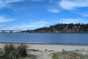 Ein Fluss mit einer Brücke, ein Sandstrand und ein bewaldeter Hang.