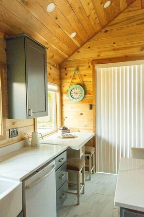 L’intérieur d’un chalet en bois comprend un espace cuisine avec un comptoir, des placards et une table à manger avec des chaises.