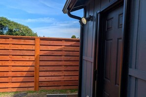 Une clôture en bois, une porte de couleur sombre et un luminaire fixé au mur.