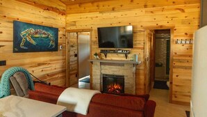 Interior acolhedor de uma cabana com lareira, uma televisão montada acima e um quadro na parede.