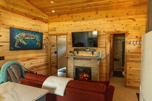 Ein gemütliches Blockhaus-Interieur mit Kamin, einem darüber montierten Fernseher und einem Bild an der Wand.