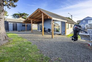 A house with a covered patio, a boat with a Suzuki outboard motor, and a gravel driveway.