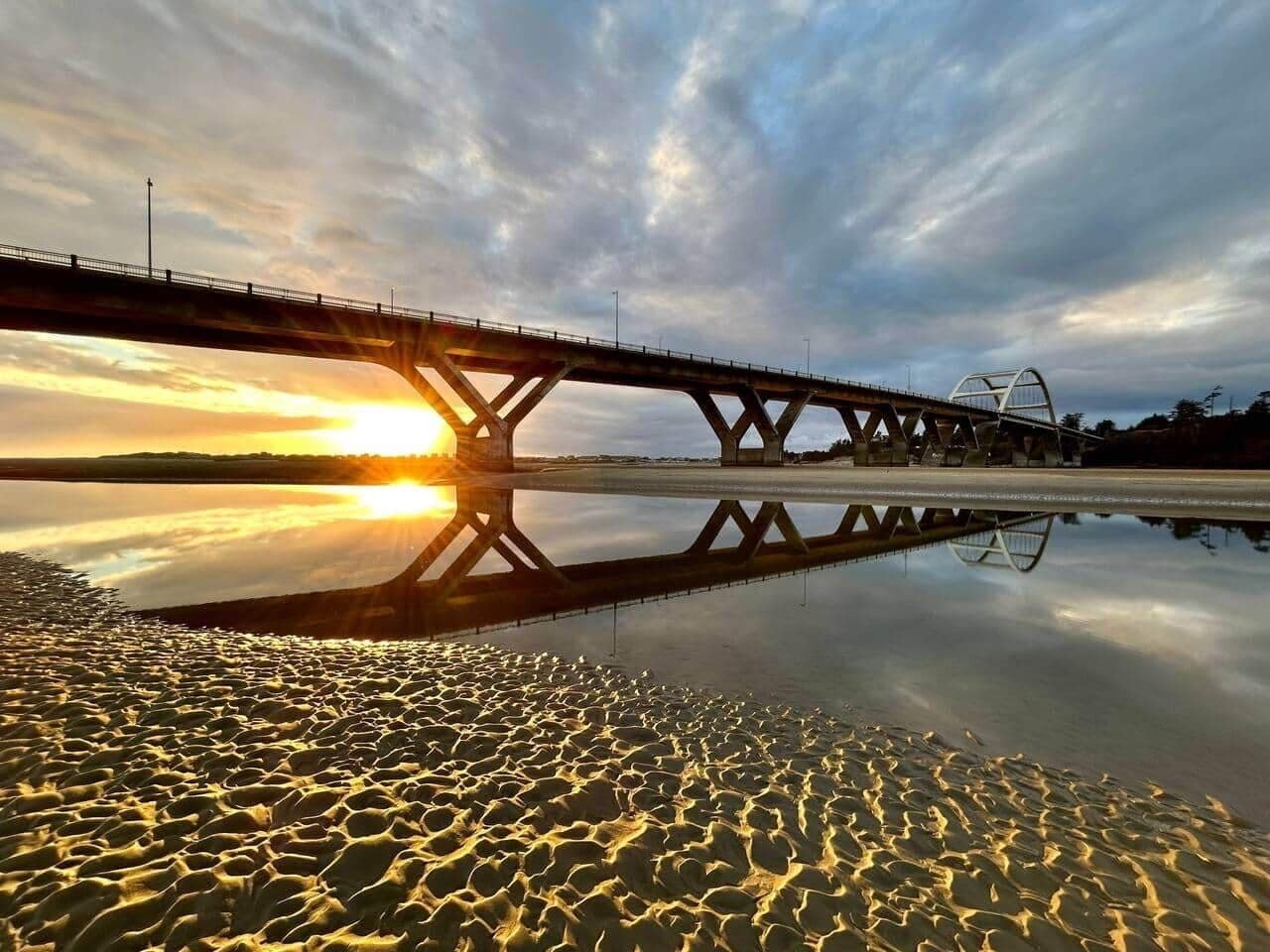 A bridge over a calm body of water with a sunset reflection.