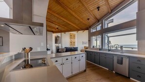 A modern kitchen with a central island, wooden ceiling, and large windows. - Devon West (Newport)