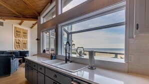 A kitchen with a large window overlooking the beach, wooden cabinets, and a modern faucet. - Devon West (Newport)